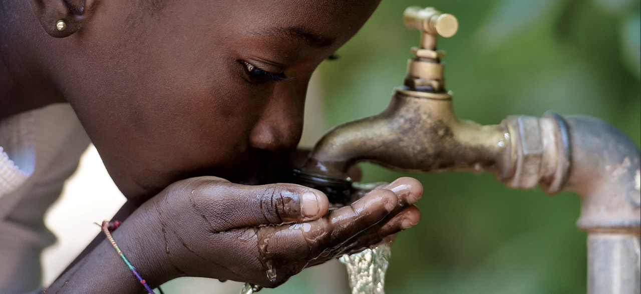 Young girl drinking from an outdoor faucet in Africa.